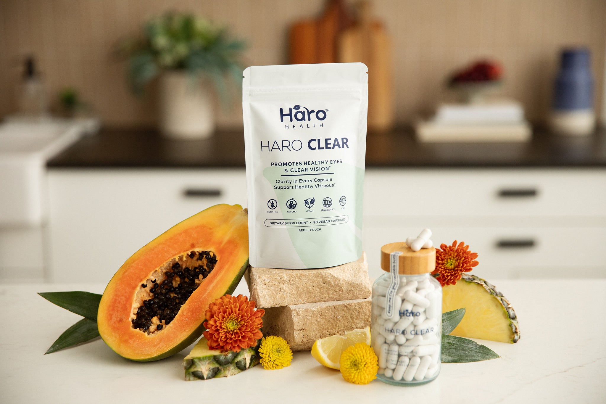 Haro Clear refill pouch and capsule-filled glass bottle with bamboo cap and two white capsules, photographed with fruit and flowers