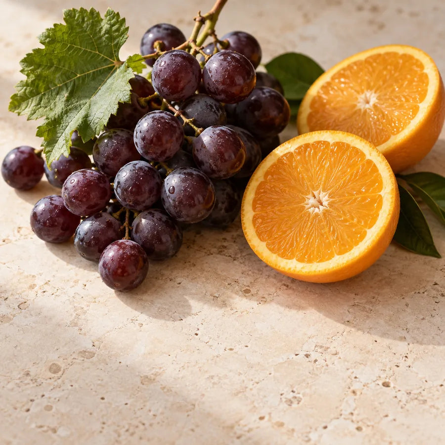 Purple grapes and fresh orange halves on a warm stone surface